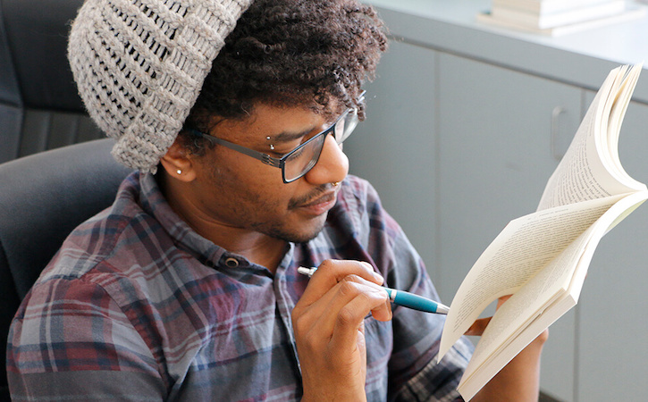 Adam Tejeda reading a book while pointing a pen at a page